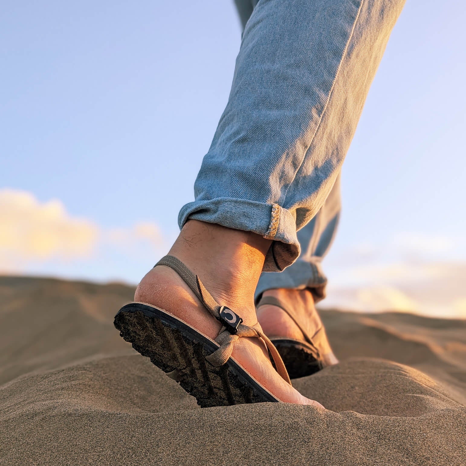 A_man_waking_up_a_sand_dune._Wearing_ZuZu_Dune_barefoot_sandals_with_a_premium_water-repellent_leather_footbed_and_recycled_desert_straps._Eco-friendly_barefoot_adventure_sandals.