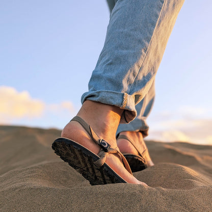 A_man_waking_up_a_sand_dune._Wearing_ZuZu_Dune_barefoot_sandals_with_a_premium_water-repellent_leather_footbed_and_recycled_desert_straps._Eco-friendly_barefoot_adventure_sandals.