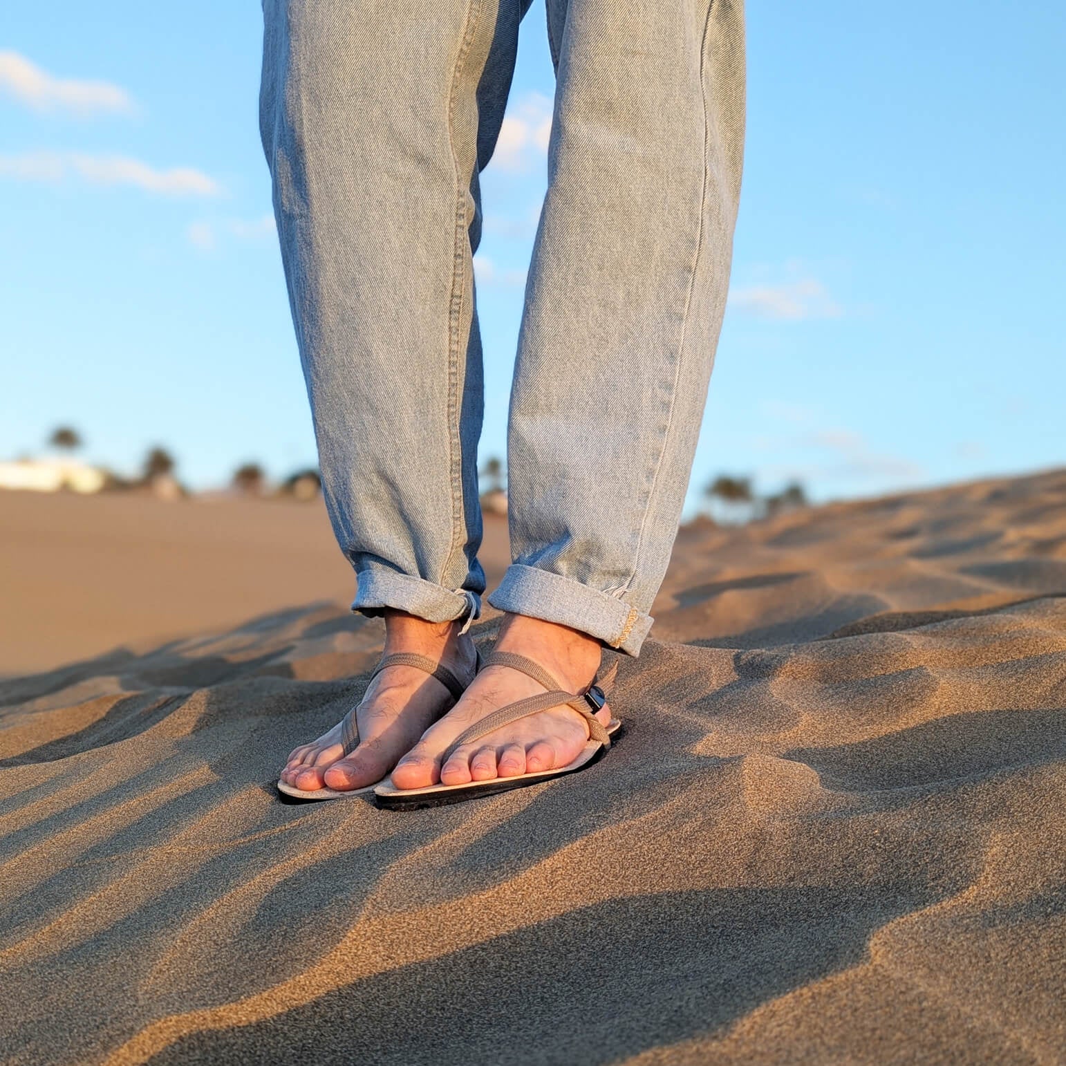 A_man_wearing_ZuZu_Dune_barefoot_sandals_with_a_premium_water-repellent_leather_footbed_and_replaceable_recycled_straps._Eco-friendly_barefoot_adventure_sandals._On_a_sandy_heel.