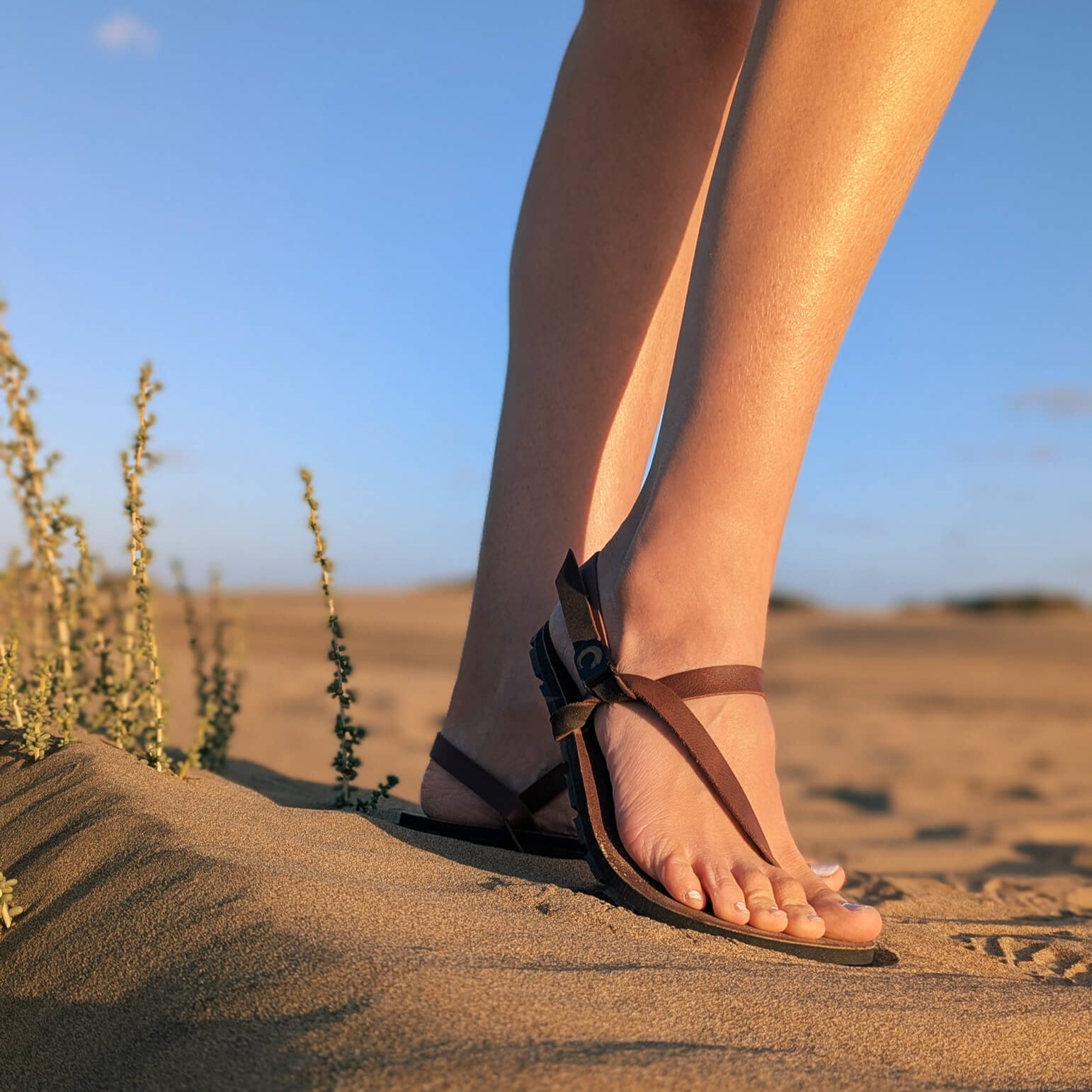 Woman_standing_on_a_sandy_hill_wearing_ZuZu_Groove_barefoot_sandals_featuring_an_antibacterial_vegan_leather_footbed_and_replaceable_recycled_straps_-_perfect_for_everyday_barefoot_li