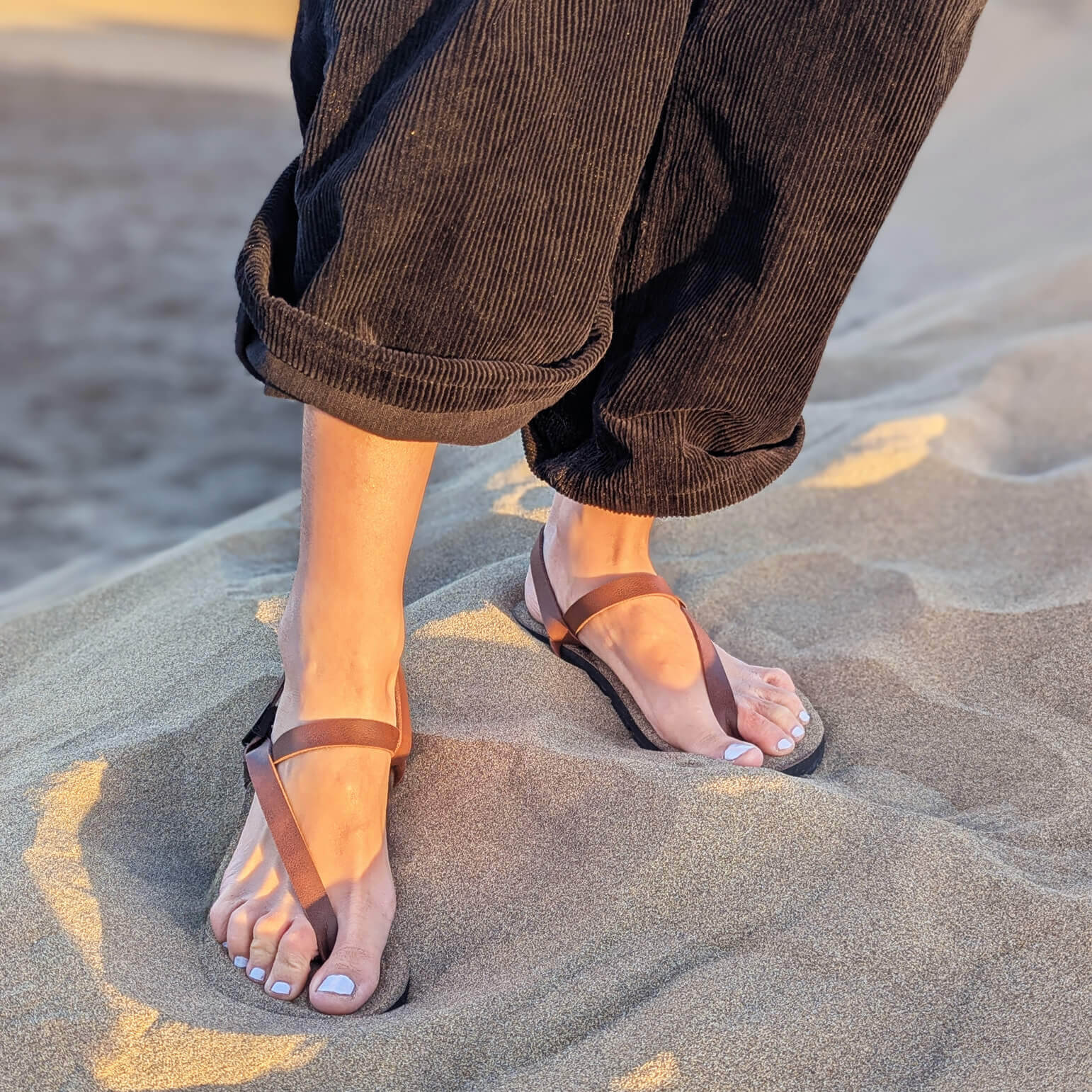 Woman_standing_on_sand_wearing_black_pants_and_a_pair_of_ZuZu_Groove_barefoot_sandals_featuring_vegan_replaceable_straps_-_perfect_for_everyday_barefoot_living