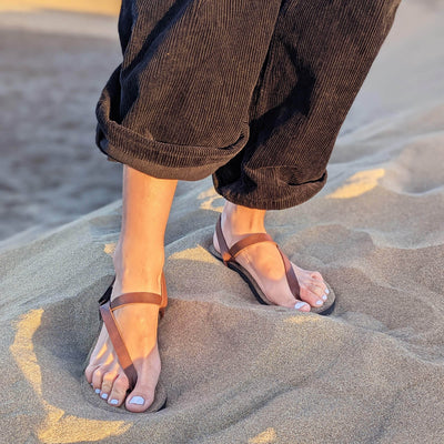 Woman_standing_on_sand_wearing_black_pants_and_a_pair_of_ZuZu_Groove_barefoot_sandals_featuring_vegan_replaceable_straps_-_perfect_for_everyday_barefoot_living