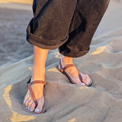 Woman_standing_on_sand_wearing_black_pants_and_a_pair_of_ZuZu_Groove_barefoot_sandals_featuring_vegan_replaceable_straps_-_perfect_for_everyday_barefoot_living